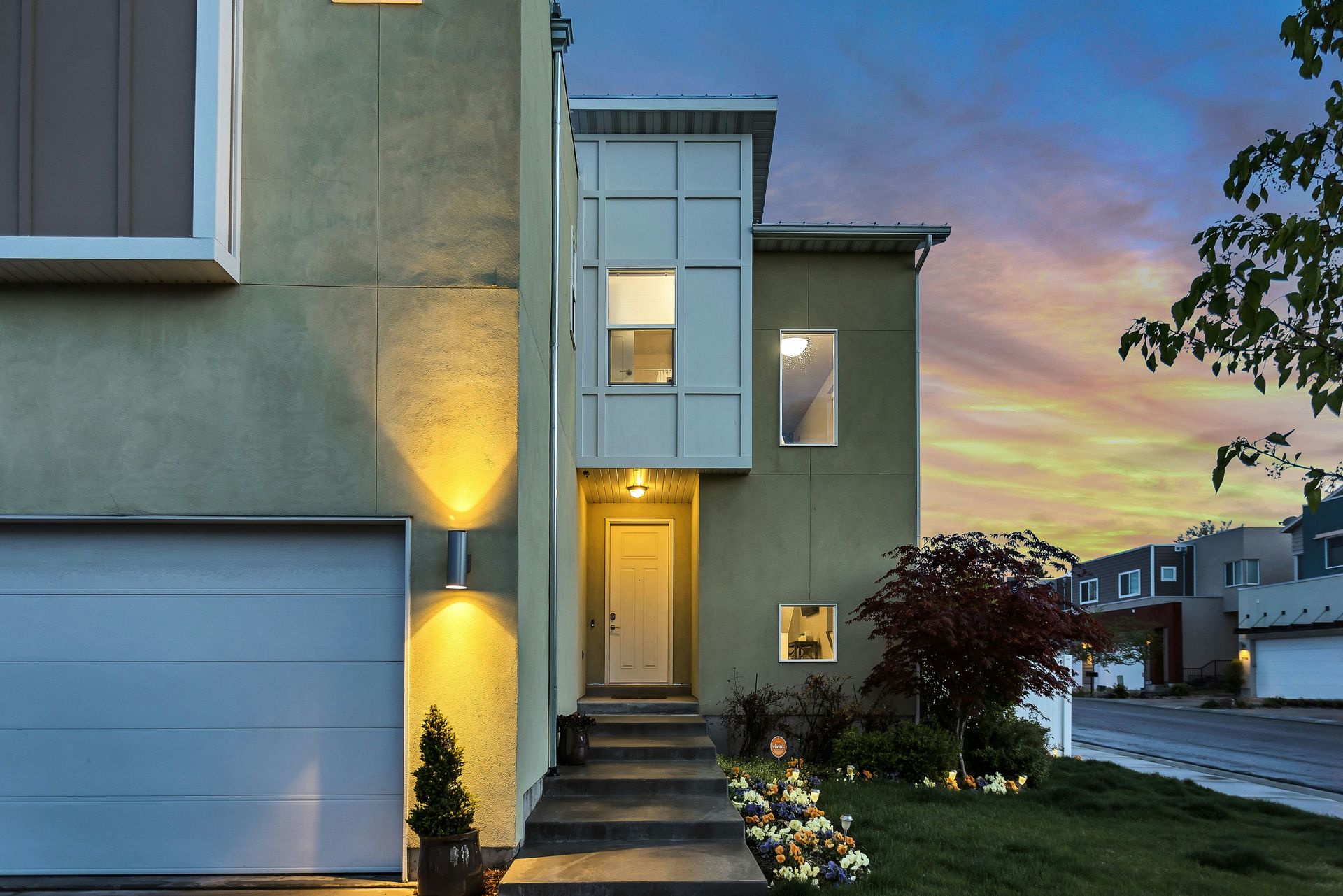A modern house with a garage and lit doorway under a colorful evening sky