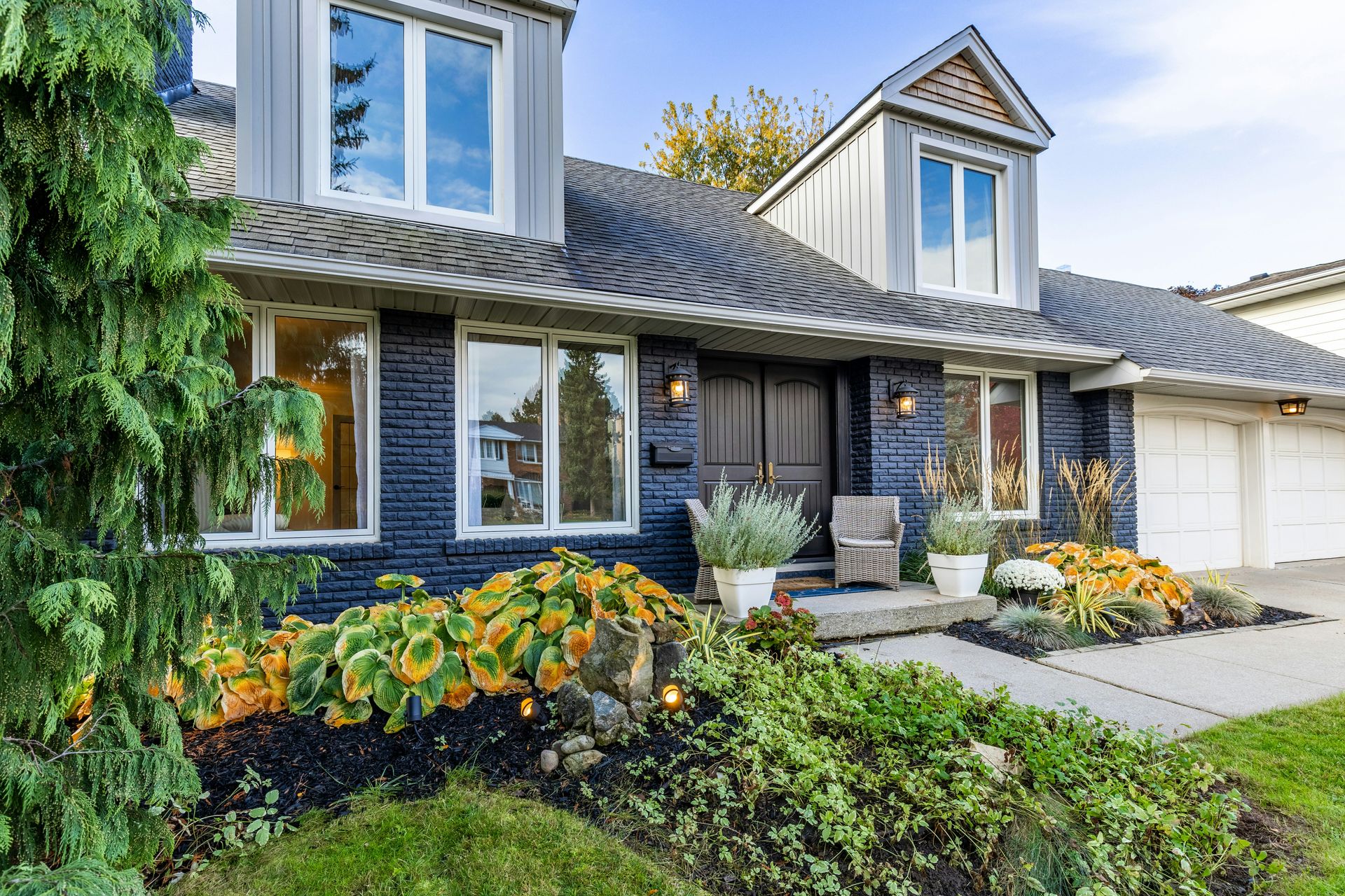 A house with dark blue brick siding and a front garden with hostas